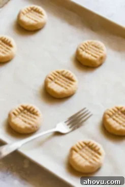 A baking sheet holding peanut butter balls pressed down with a fork to get the criss cross pattern.