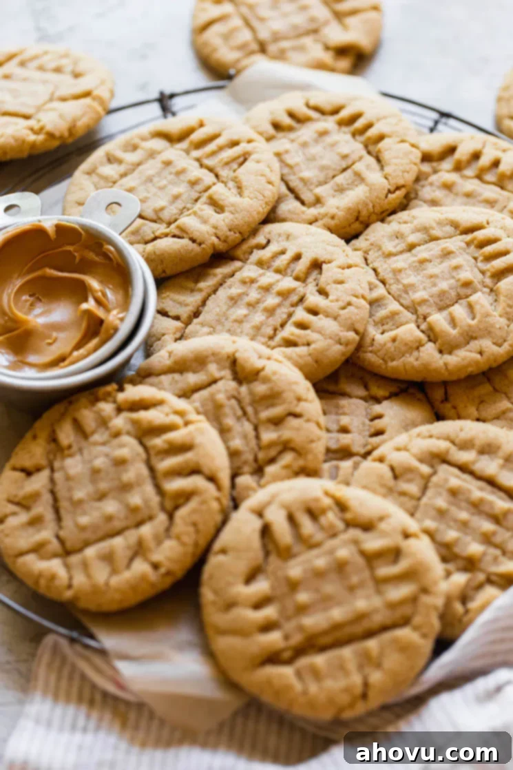 A round cooling rack holding peanut butter cookies piled on each other with a small metal cup of peanut butter off to the side.