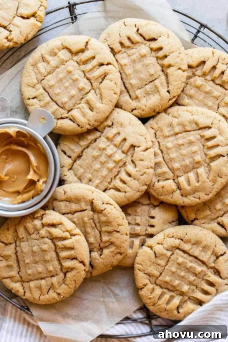 An overhead view of peanut butter cookies on a round cooling rack with a metal cup of peanut butter off to the side.