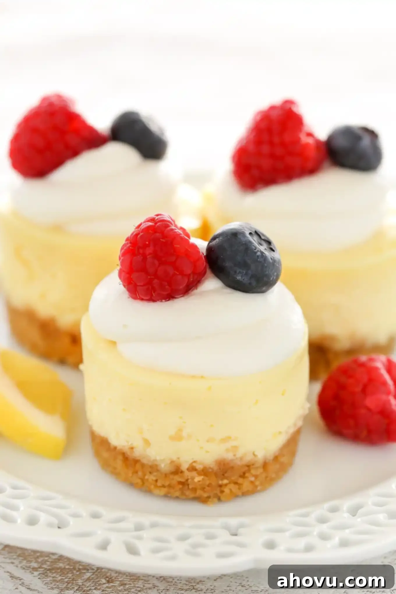 Three mini cheesecakes with a graham cracker crust on a white plate. Each mini cheesecake is garnished with whipped cream and fresh berries. 