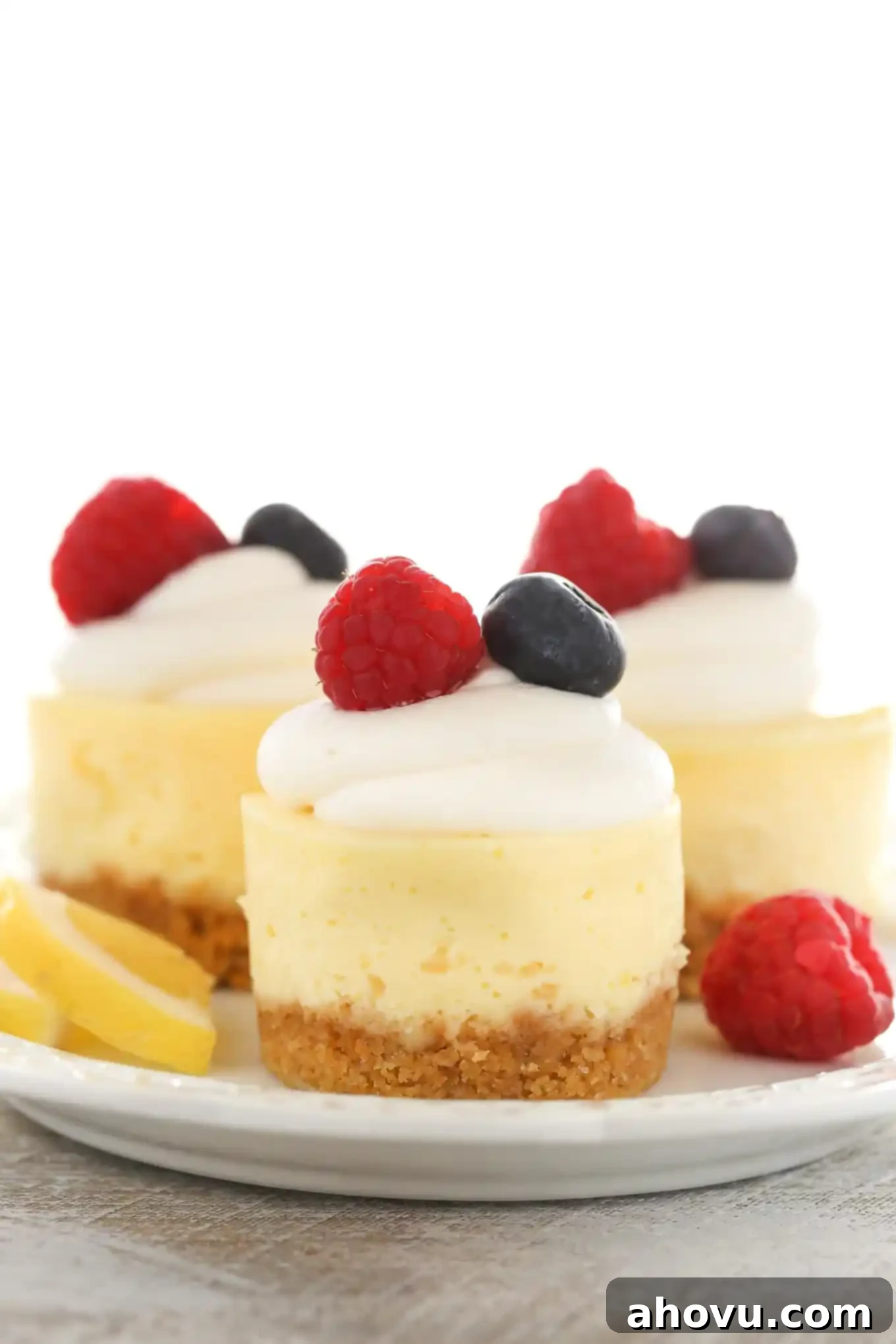A side view of three lemon cheesecake bites on a white plate. Each is topped with whipped cream and fresh berries. 