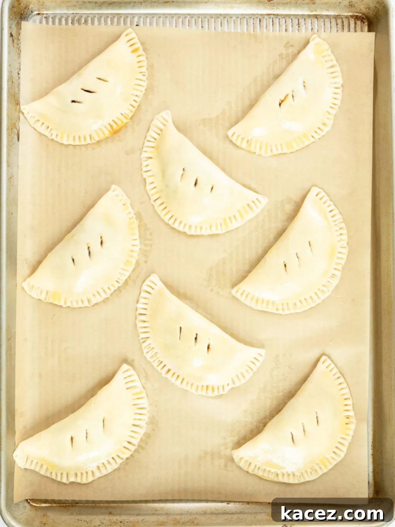 Spiced Pumpkin Pastries 8 Unbaked pumpkin hand pies neatly arranged on a lined baking sheet, chilled and ready for the oven.