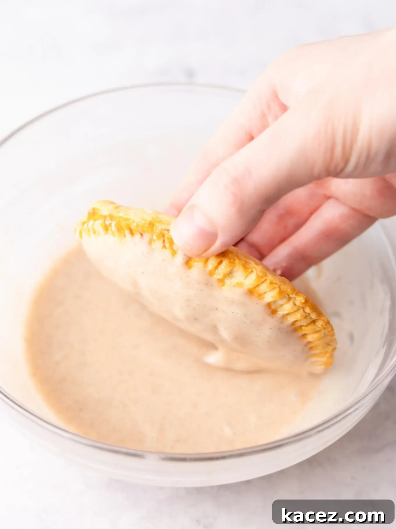 Spiced Pumpkin Pastries 9 A baked pumpkin hand pie being dunked into a bowl of pumpkin spice glaze.