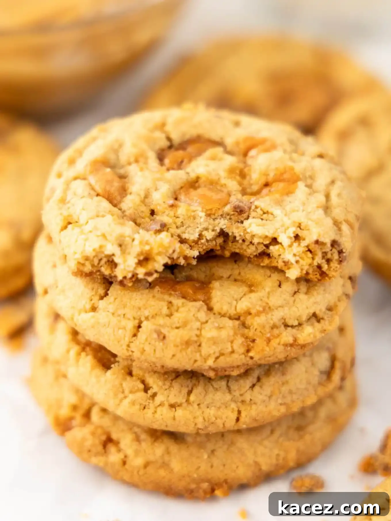 Sweet & Crunchy Butterfinger Treats 8 A stack of golden-brown Butterfinger cookies, with the top cookie having a bite taken out of it, revealing its soft interior and crunchy candy pieces.