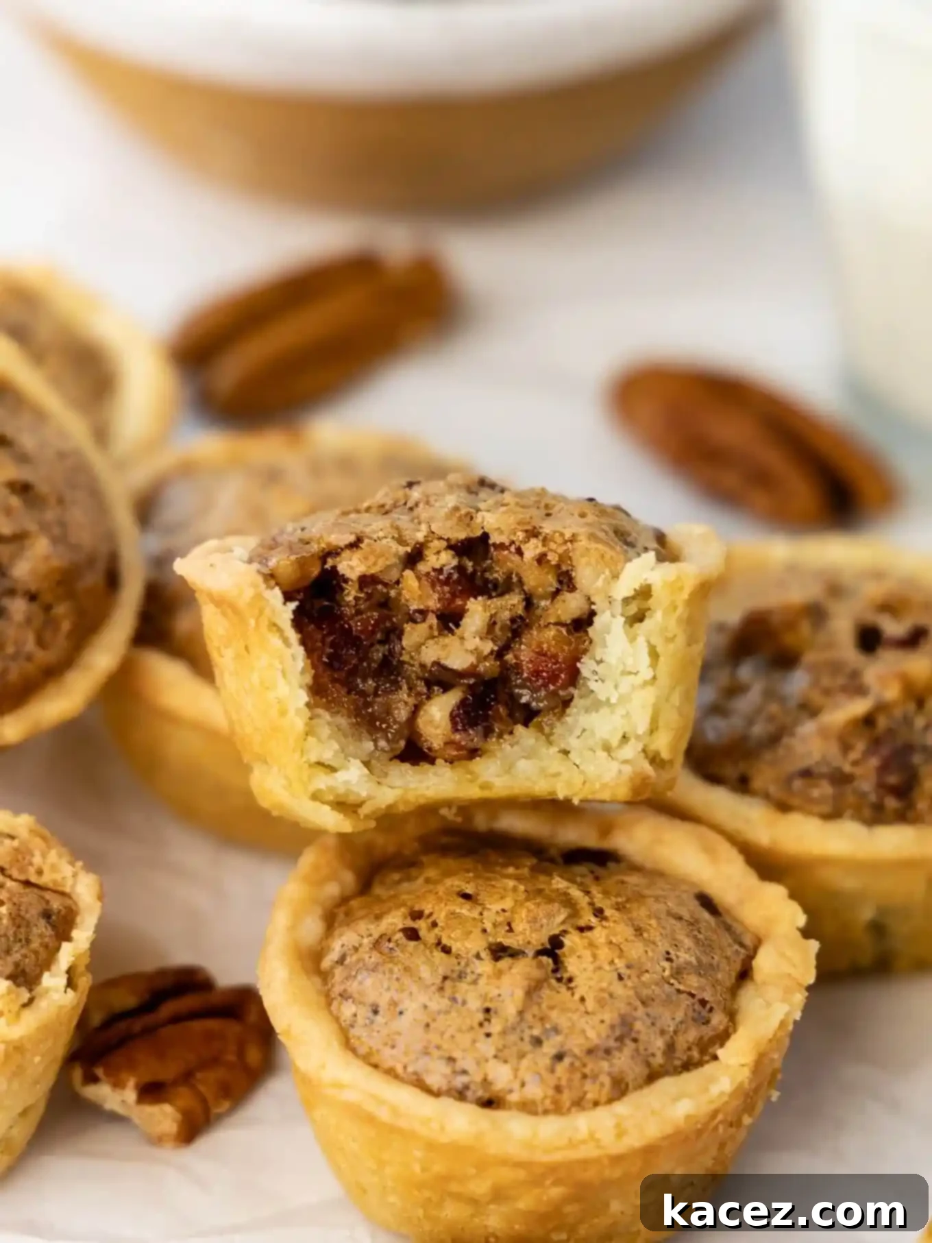 Bite-Sized Pecan Perfection 2 A beautifully arranged pile of golden-brown pecan tassies, with one tempting bite missing from the top treat, showcasing the rich pecan filling.