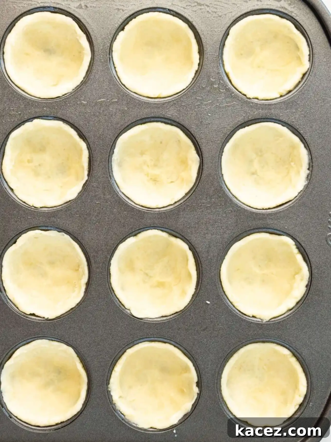 Bite-Sized Pecan Perfection 5 A close-up, overhead view of the cream cheese crust perfectly pressed into the individual cavities of a mini muffin pan, showcasing its readiness for filling.