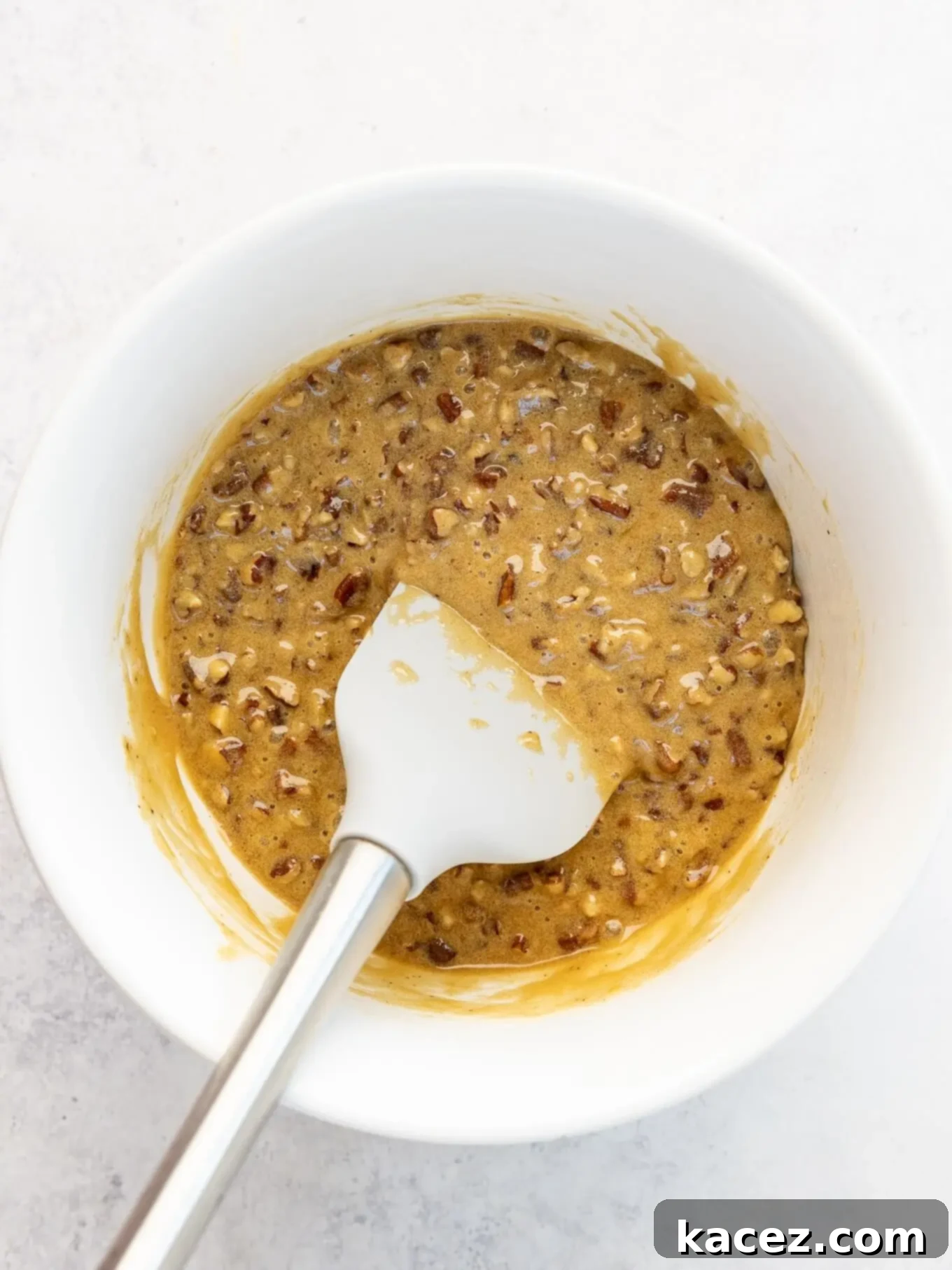 Bite-Sized Pecan Perfection 6 An overhead view of the luscious pecan filling mixture in a white mixing bowl, with a spatula resting in it, ready to be scooped.