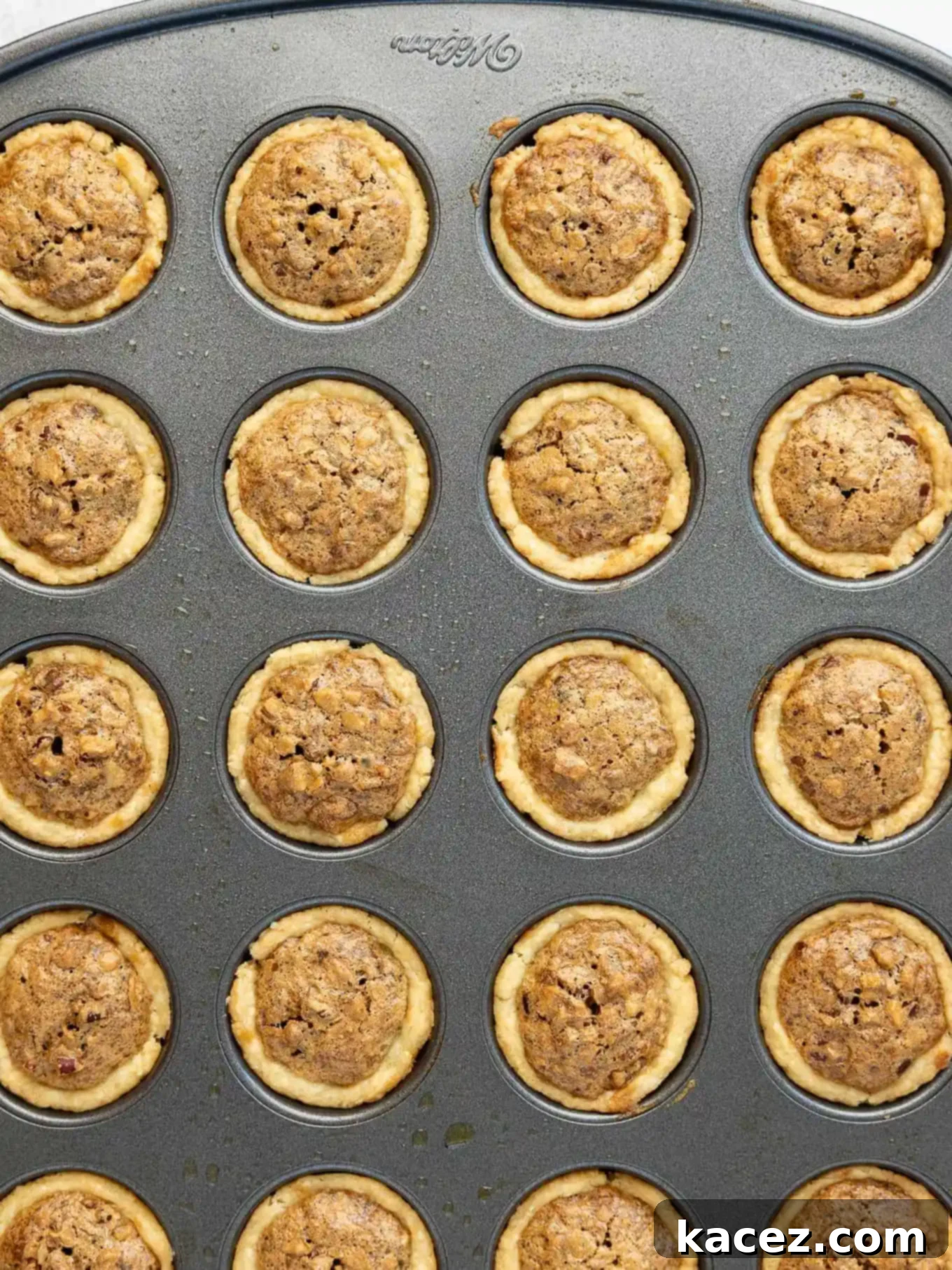 Bite-Sized Pecan Perfection 7 An overhead shot of baked pecan tassies still in a mini muffin pan, showcasing their golden-brown tops and rich filling, cooling after baking.