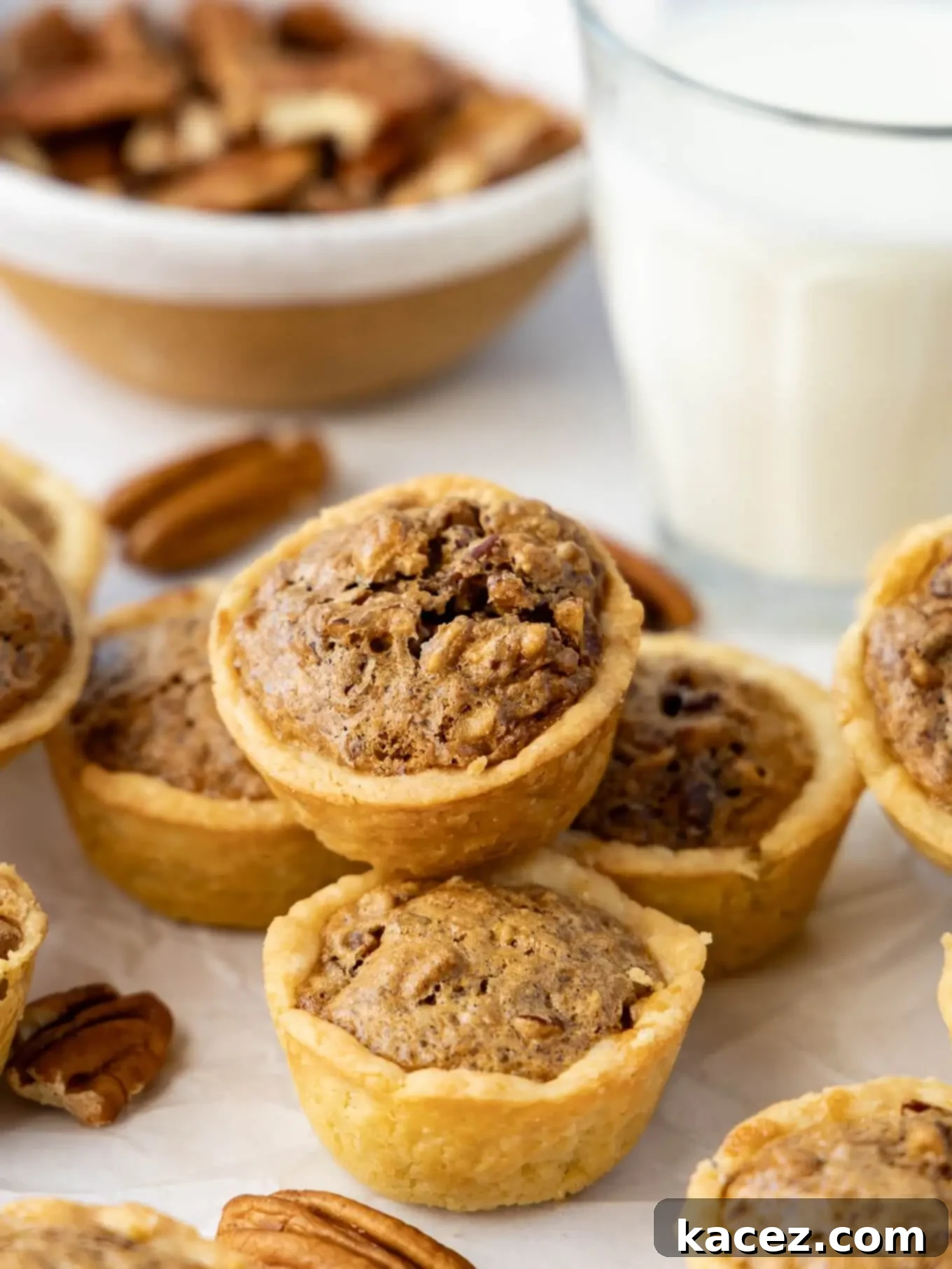 Bite-Sized Pecan Perfection 8 A charming pile of golden-brown pecan tassies, artfully surrounded by whole pecans, ready to be enjoyed.