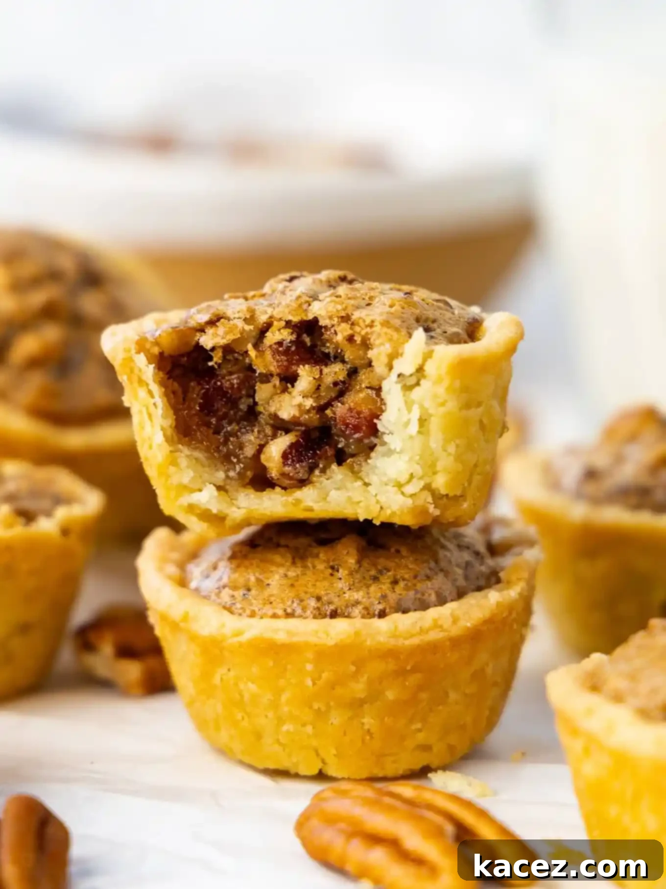 Bite-Sized Pecan Perfection 9 Two perfectly baked pecan tassies stacked one on top of the other, with a corner bite missing from the top tassie, revealing its delicious interior.