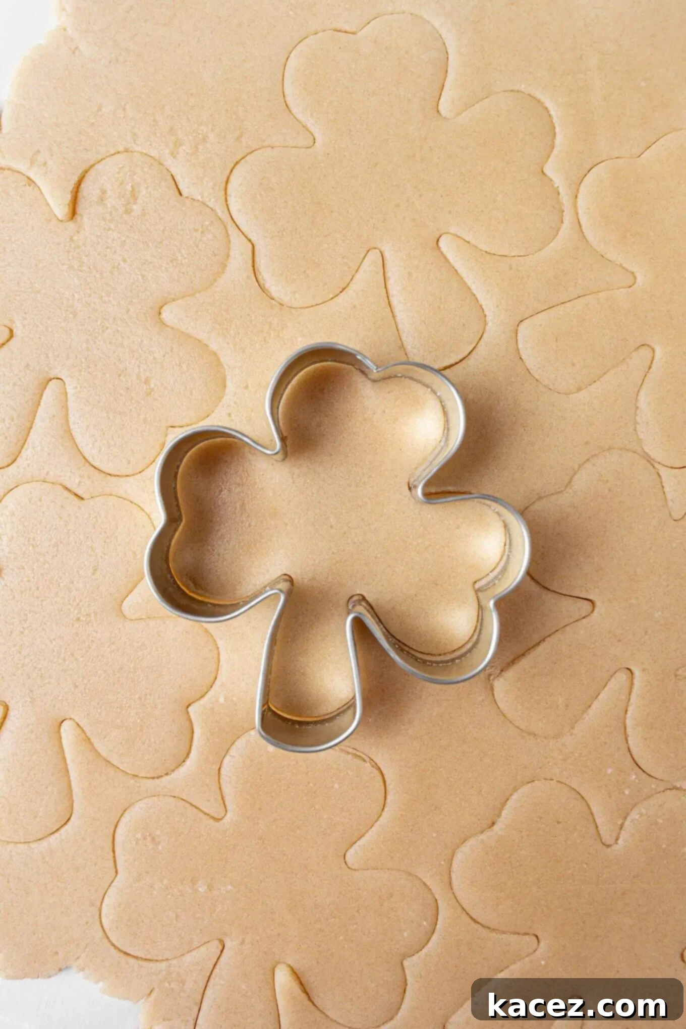 Sharp shamrock-shaped cookie cutter pressing into the rolled-out sugar cookie dough, creating perfect St. Patrick's Day cookies.